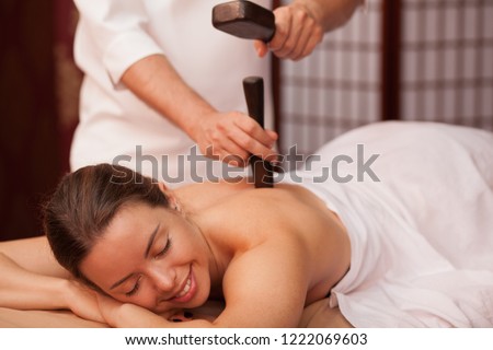 Gorgeous woman smiling with her eyes closed enjoying traditional thai hammer massage at spa center. Beautiful happy woman receiving tok sen massage by professional masseur. Travel, health concapt