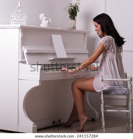 The beautiful girl  sits on a chair about the white piano in a studio