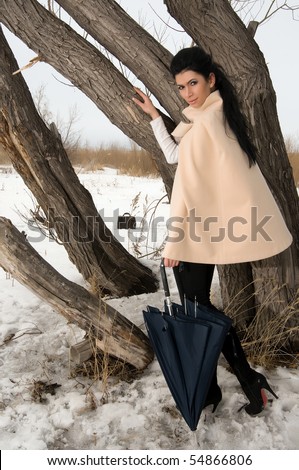 The lonely beautiful girl costs near a tree in the street, in hands holds an umbrella.