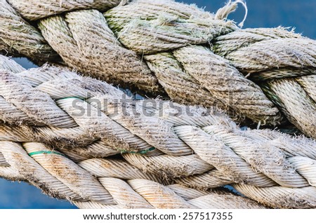 Close-up of a mooring rope with a knotted end tied around a cleat on a pier/ Nautical mooring rope