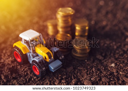 Agricultural tractor toy and golden coins on fertile soil land, income from activity in agriculture or investment and bank loans for farm development