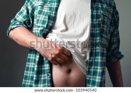 Beer belly of adult man. Casually dressed man is scratching his small beer belly.