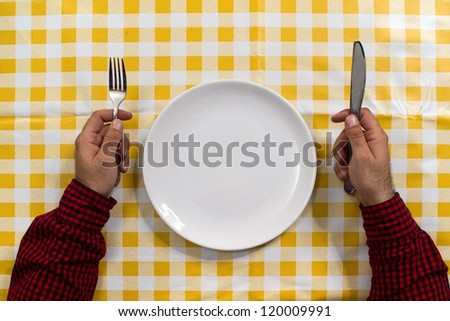 Hungry man. Man sitting at the dinner table with fork and knife and empty plate