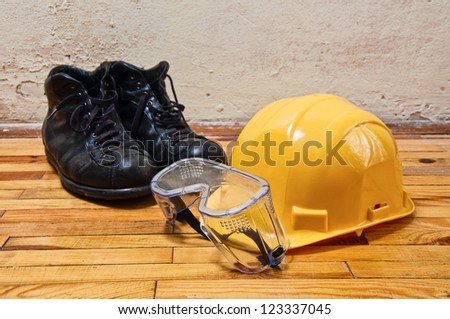 Yellow hard hat, old leather boots and protective goggles, protective equipment in construction industry.