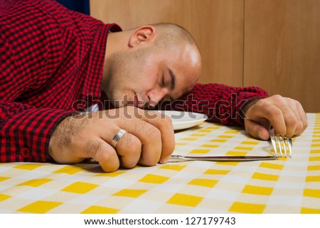 Young adult bold man sleeping at the dinner table with fork and knife in his hands