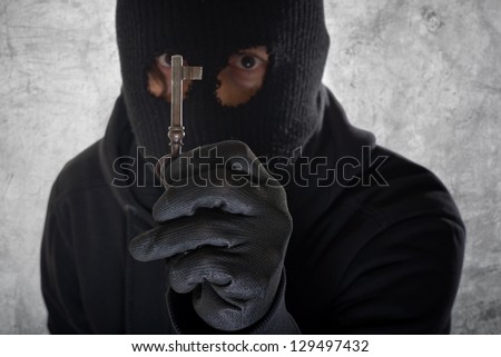 House burglar with balaclava holding vintage house key.