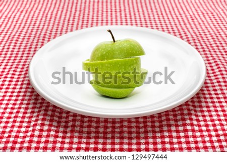 Green apple on white plate. Sliced green smith apple on a white ceramic plate on red and white checkered tale cloth.