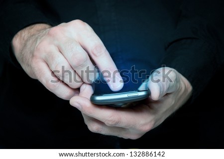 Man in black shirt is typing a text message on his smartphone, close up image, focus on hands and the phone device.