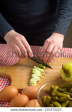 Female hands cutting leek on a wood chop board with black ceramic knife.