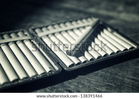 Cigarettes in cigarette case on wood table. Day light with dark shadows.
