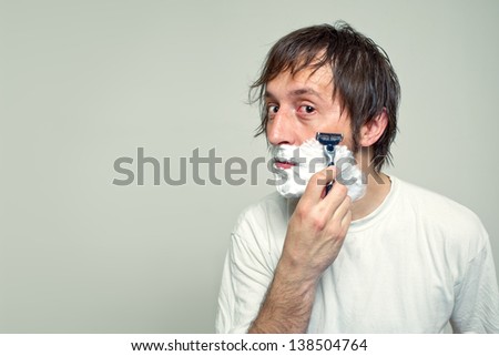 Man shaving in the bathroom, looking at the mirror.