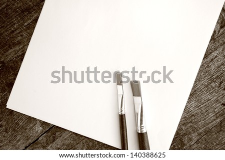 Paint brushes and blank white paper on old wood background.