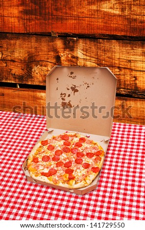 Pepperoni pizza delivery. Tasty pizza with pepperoni sausage in white cardboard box on kitchen table