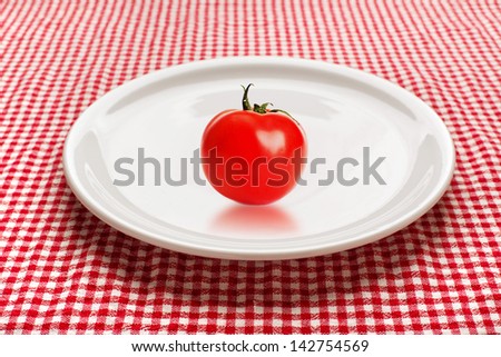 red tomato on a white plate on kitchen table. Organic food and dieting concept.