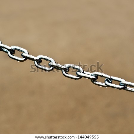 Steel chain link over brown background, shallow depth of field.