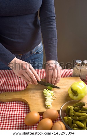 Female hands cutting leek on a wood chop board with black ceramic knife.