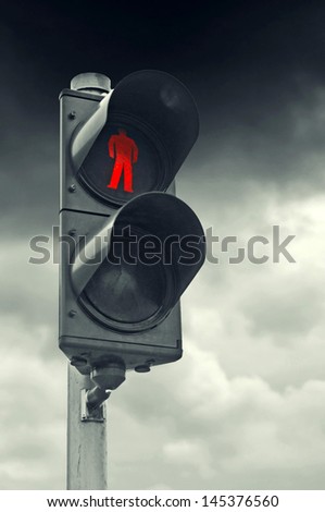 Red traffic light for pedestrians against gray cloudy sky. Stop obligation.
