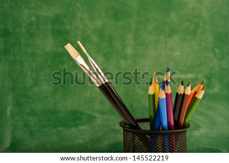 Color pencils in pencil box, green chalkboard in background