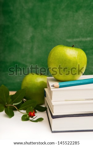School books, apple and pencil, chalkboard in background.