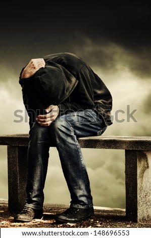 Man with problems. Man in hood with hands on his head sitting on the concrete bench. Drug addict concept.