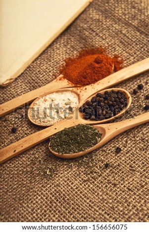 Spices. Food ingredients on wood spoons with open book on kitchen table.