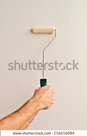 Man painting an interior wall of the room with paint roller