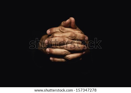 Male hands crossed for prayer in dark