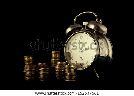 Golden coin stack and vintage clock on dark background. Time is money concept.