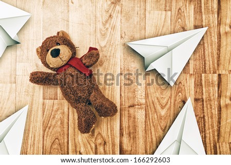 Cute bear toy on laminated wooden floor with paper origami planes, top view