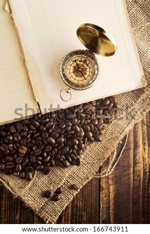 Coffee beans and compass on open book on jute canvas texture, top view