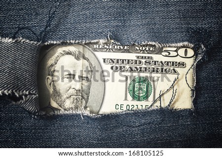 Fifty dollars bill through torn blue jeans texture. American economy concept.