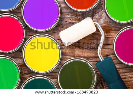 Small paint roller and color tin cans on old wood background. Redecoration and renovation concept, top view
