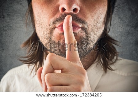 Businessman making hush gesture, finger on mouth for silence.
