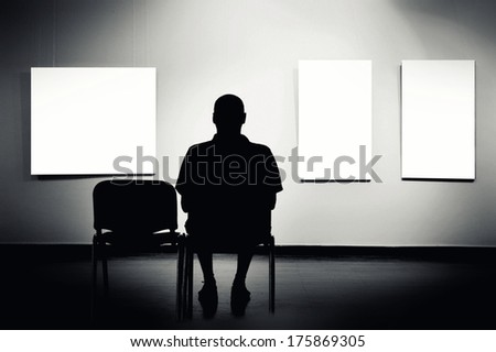 Man Sitting In Art Gallery, Looking At Art Displayed On Walls.