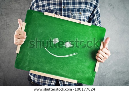 Smiling emoji. Man holding green chalkboard with smiley face drawing