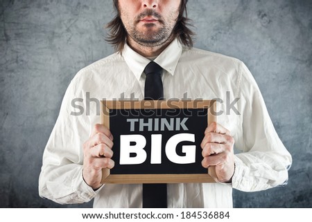 Businessman holding blackboard with THINK BIG title. Business concept.
