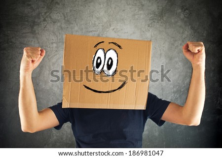 Happy smiling man with cardboard box on his head and raised fists for victory. Concept of winning.