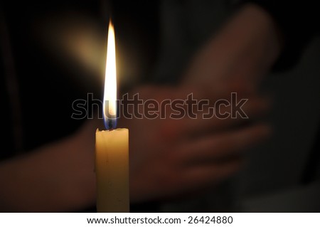 Candle burning, crossed women hands in the background.