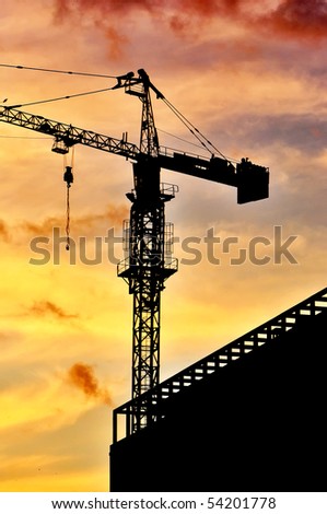 Dark silhouette of a construction crane at dusk, against warm orange sky.