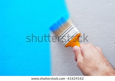 Man is holding a brush and painting a white wall