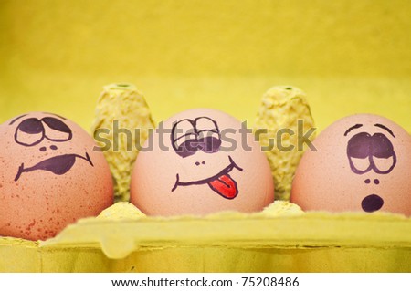 Funny easter eggs fresh eggs with drawn faces depicting various emotions arranged in a cardboard egg carton against white.