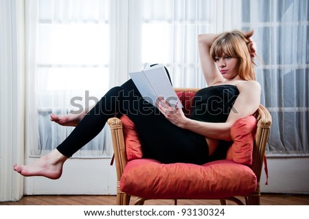 Young woman is reading a book, sitting in the chair