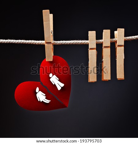 Heterosexual couple breaking apart, conceptual love image of paper heart ripped in two, hanging on rope with clothes pin.