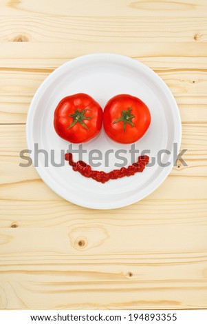 Fun food for children - tomatoes and ketchup making smiley face served on a white plate on wooden table.