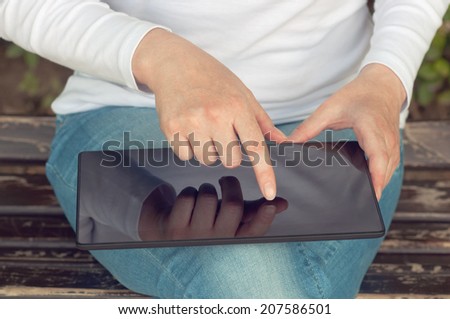 Woman using digital tablet computer and browsing the internet while sitting on a wooden bench in the park.