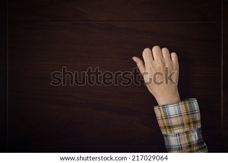 Female hand is knocking on wooden door, conceptual image. Visitor or guest is at the door.