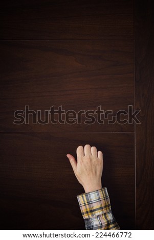 Female hand is knocking on wooden door, conceptual image. Visitor or guest is at the door.