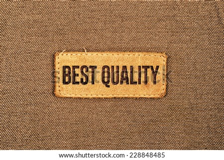 Best Quality Leather Label Tag on cotton fabric texture background, top view