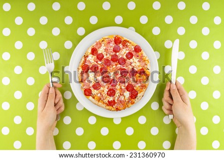 Woman eating pizza. Caucasian Female hands at dinner table holding fork and a knife above plate with served pepperoni pizza.