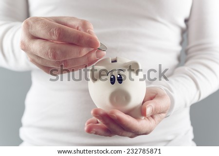 Woman putting coin in piggy coin bank, selective focus with shallow depth of field